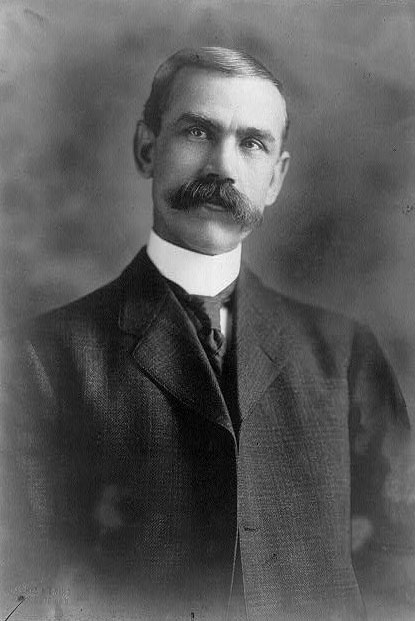 Head-shot portrait of Senator Smoot with a mustache in a dark suit with a high collar